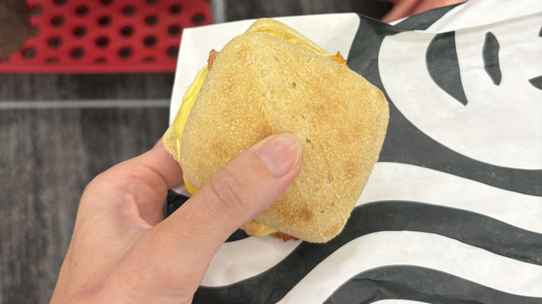 A person holding a bacon, egg, and Gouda sandwich from Starbucks
