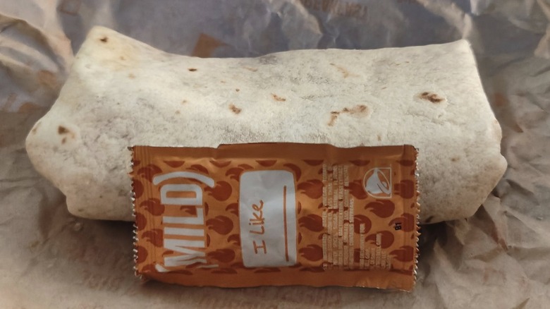 A packet of Taco Bell Mild Sauce next to a burrito
