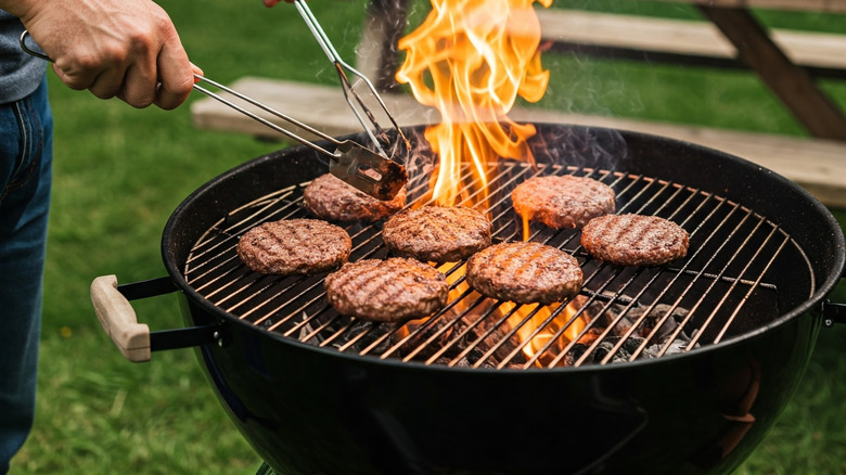 Person cooking burgers on a charcoal grill