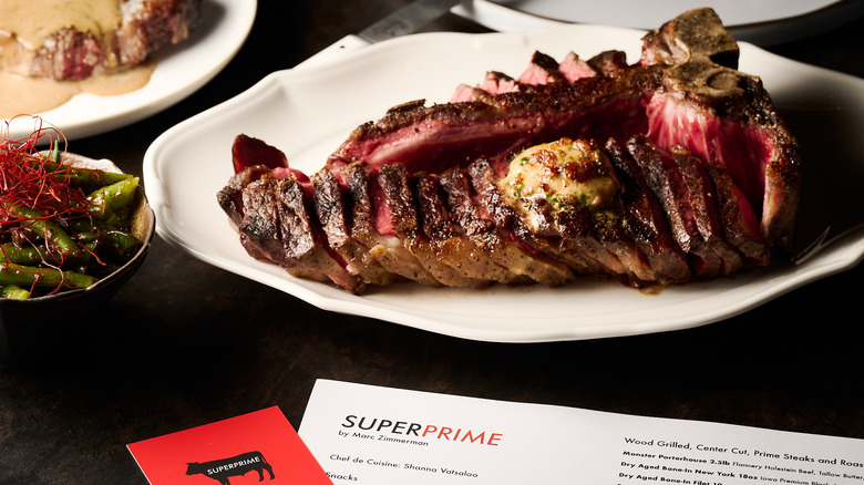 Steak from Superprime Steakhouse on a table next to a dish of vegetables and a menu