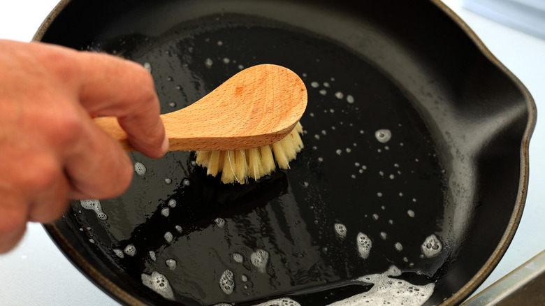 Person scrubbing cast iron skillet with brush