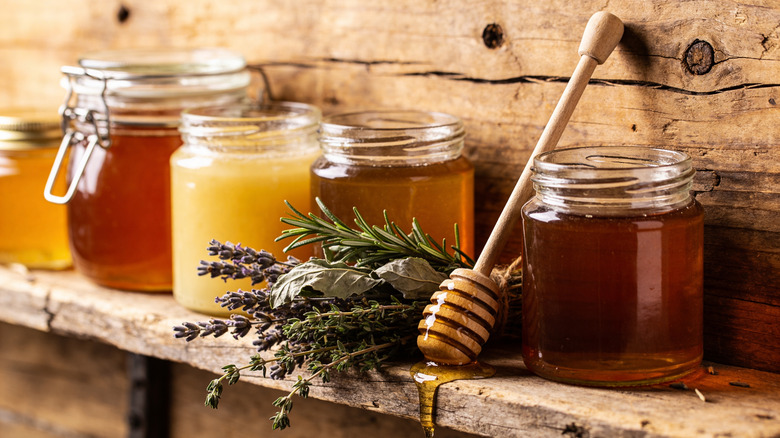 Assorted honeys on a rustic ledge with fresh herbs