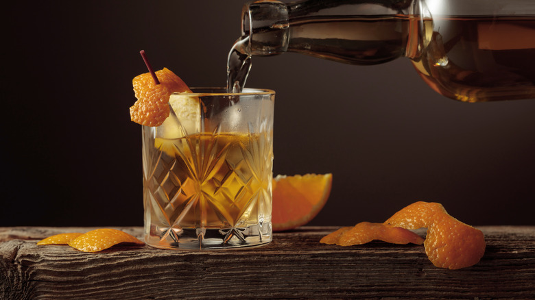 Pouring a drink in a glass on a wooden surface surrounded by orange peels