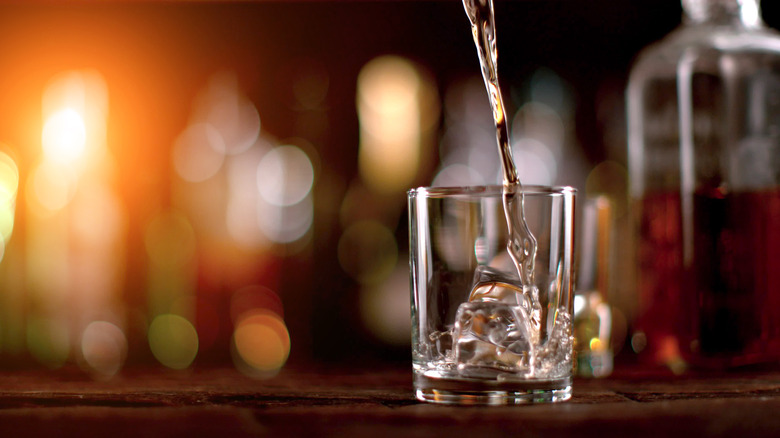 Pouring water into a glass behind spirit bottles on a counter