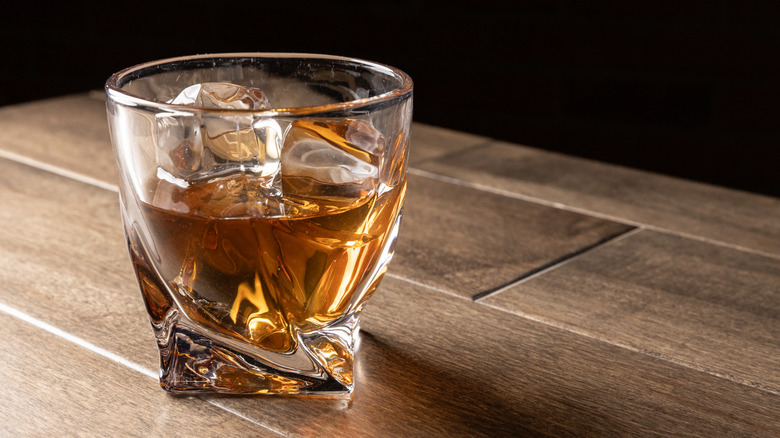 Two glasses of whisky with ice next to an old wood barrel
