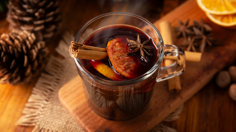 Hot mulled wine in a glass surrounded by winter-themed decor, spices, and citrus slices