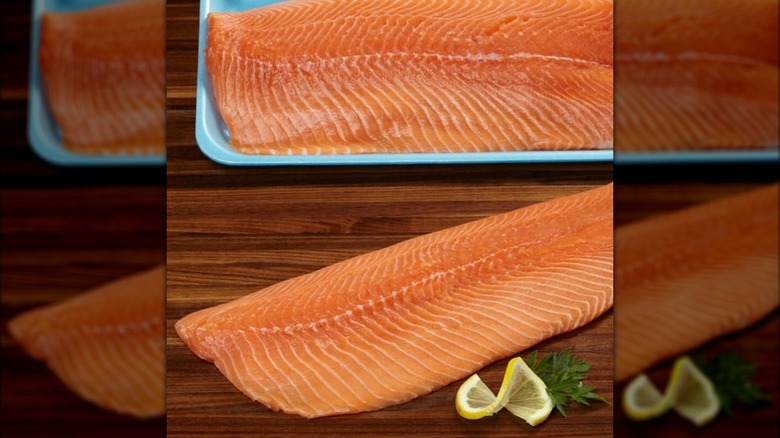 A blue package of fresh salmon next to a salmon filet on a cutting board with a lemon slice
