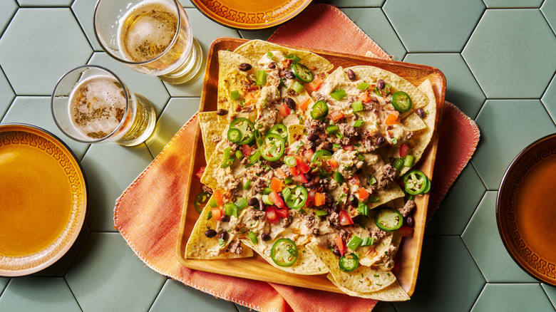 A plate of nachos on a table with two beers at a restaurant