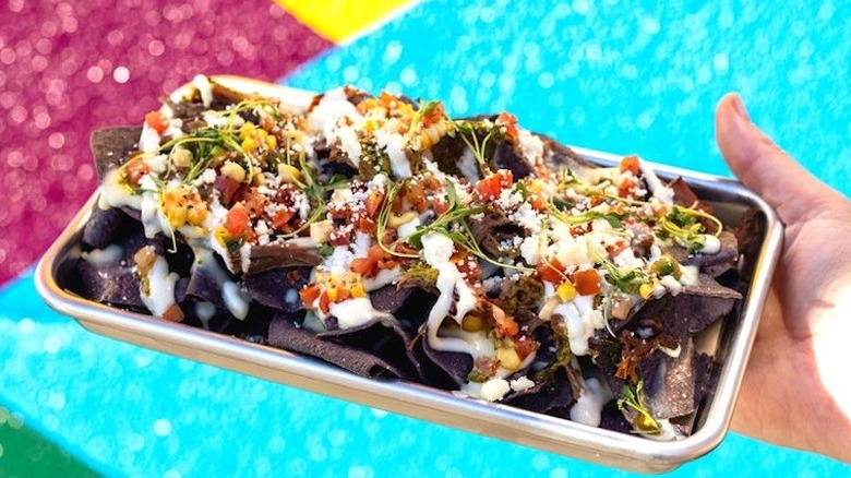 A person holding a tray of brisket nachos at Velvet Taco