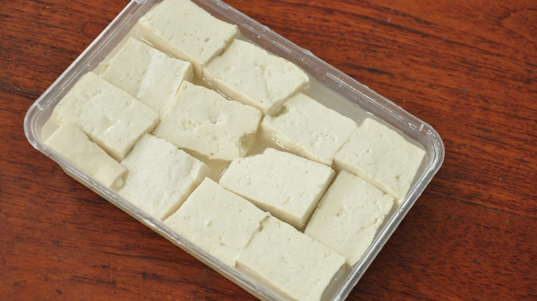 container of tofu in water on wooden table