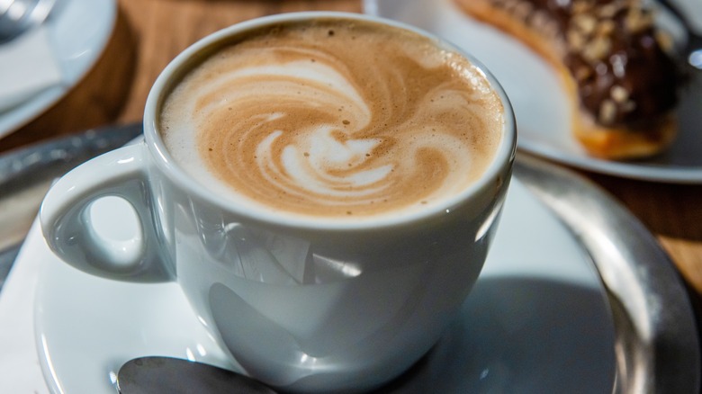 A latte sits in a white mug on a white plate