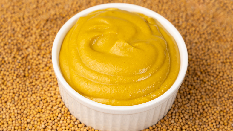 Honey mustard in white ramekin atop mustard seeds