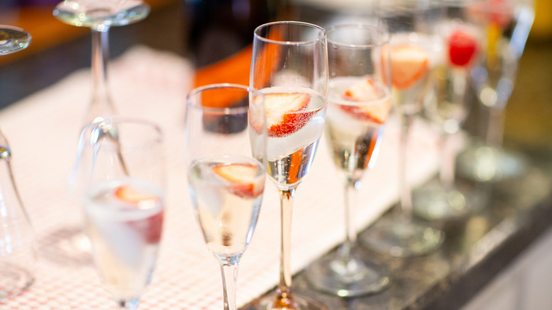 multiple flutes in a row filled with champagne and garnished with strawberries