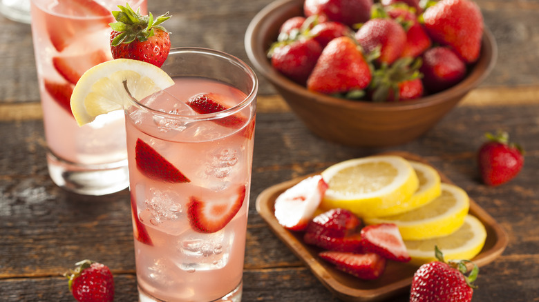 Glasses of strawberry lemonade next to plates and bowls of fresh fruit