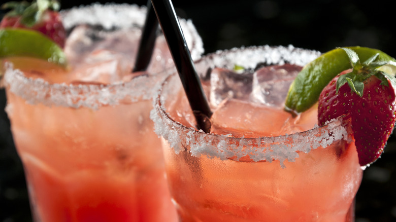 Two strawberry Margaritas with straws, a salt rim, and a garnish of a lime wedge and strawberry