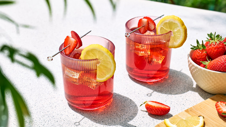 Two rocks glasses with lemon wedges and spears of strawberry slices next to a bowl of strawberries