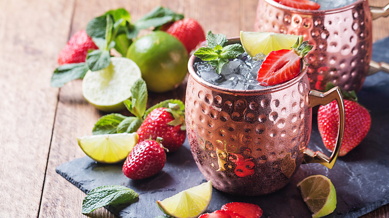 Two Moscow Mule cocktails on a slate surrounded by fresh mint, strawberries, and limes