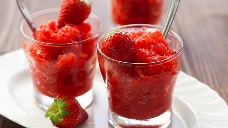 Two glasses with strawberry slushes served with whole berries and metal spoons