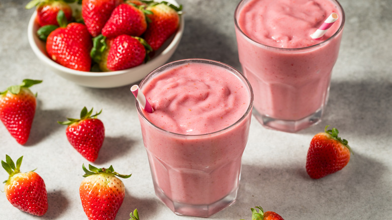 Two thick strawberry shakes with straws next to fresh strawberries