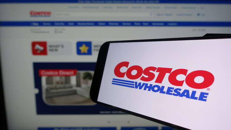 An image of a smartphone and a blurred Costco webpage behind it