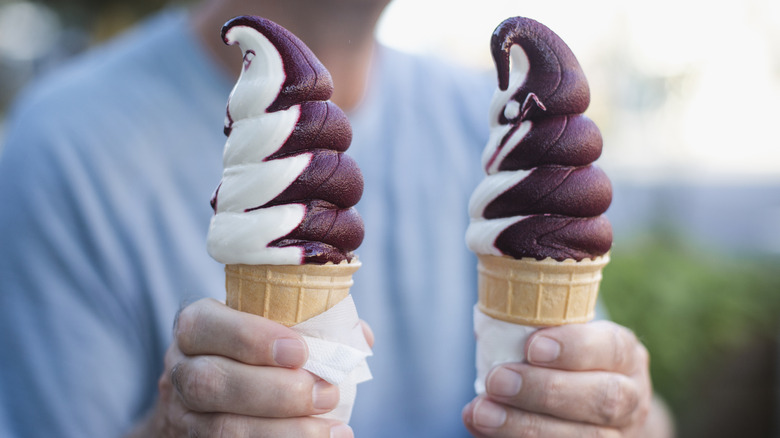 a man holding two cones of soft-serve ice cream