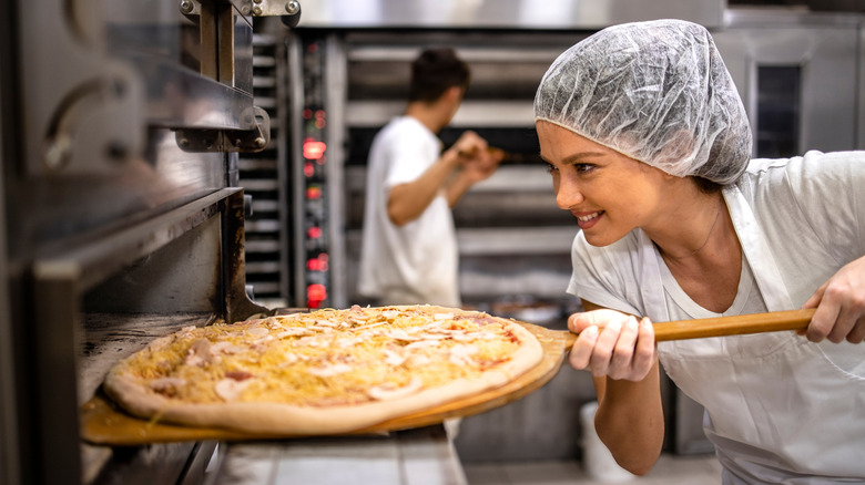 a food court worker sliding an unbaked pizza into an oven