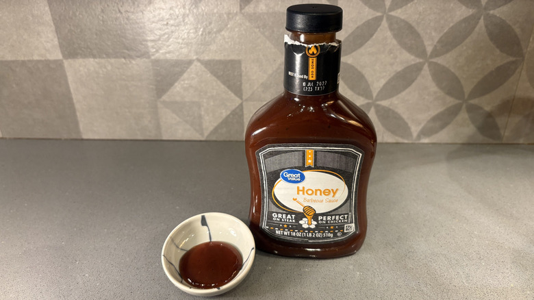 A bottle of Great Value Honey BBQ near a small cup of sauce