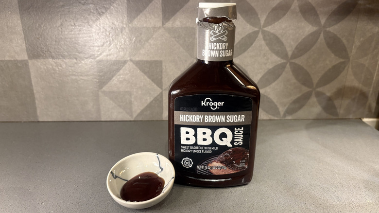 A bottle of Kroger Hickory Brown Sugar BBQ near a small cup of sauce