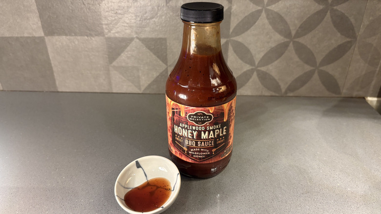 A bottle of Private Selection Applewood Smoke Honey Maple BBQ near a small cup of sauce