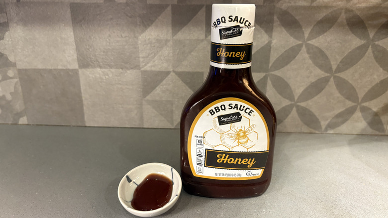 A bottle of Signature Select Honey BBQ near a small cup of sauce