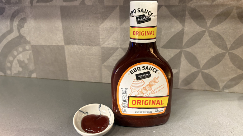 A bottle of Signature Select Original BBQ near a small cup of sauce