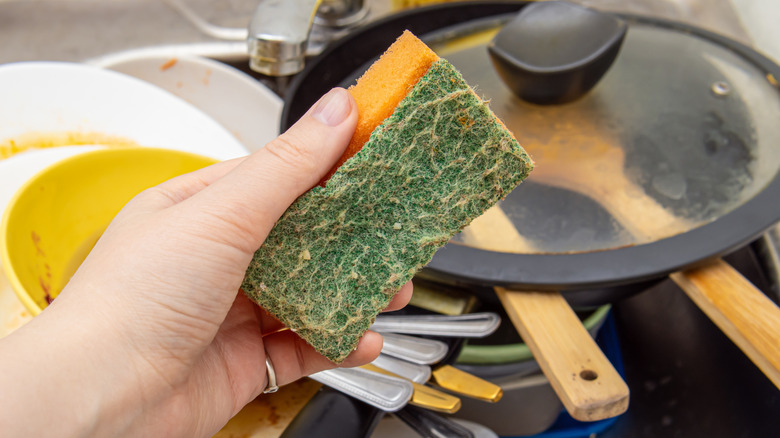 Someone holding a dirty sponge in front of dirty dishes