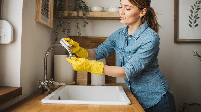 A woman wearing gloves scrubbing her faucet