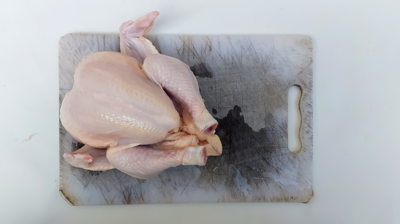 A whole raw chicken on a scratched cutting board