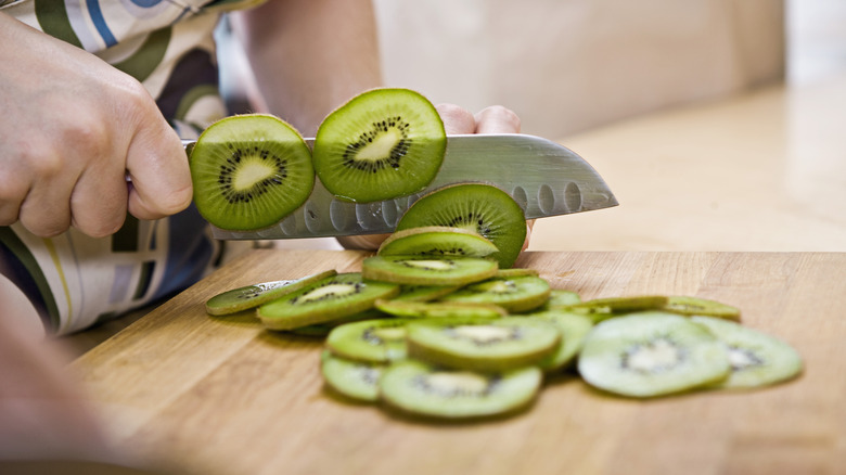 Person chopping a kiwi on a cutting board