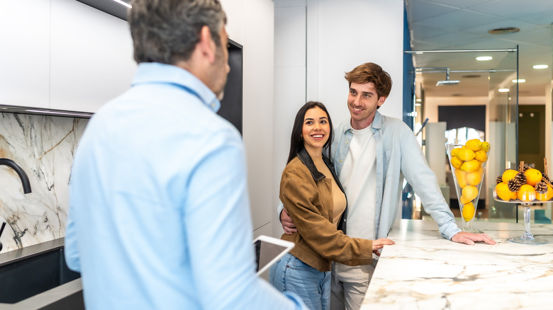 A smiling couple discusses their home's kitchen countertop with a contractor