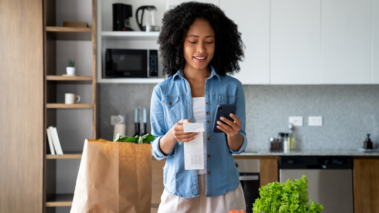 A woman checks her order in her kitchen after receiving a grocery delivery