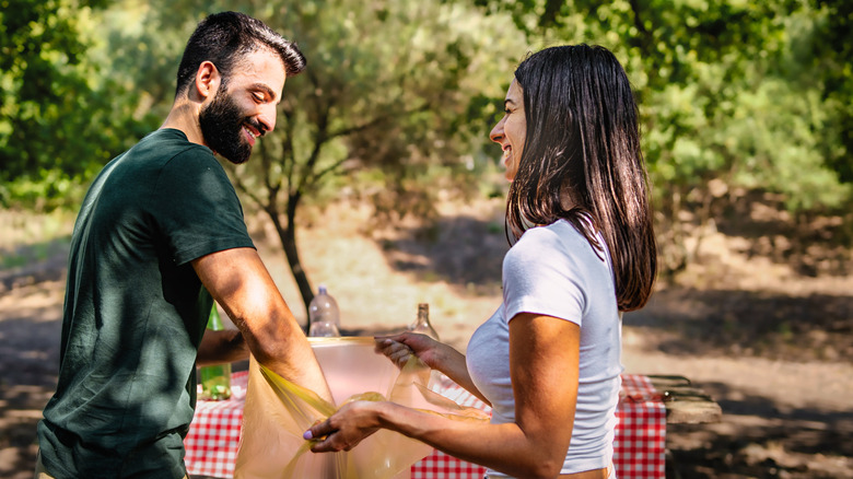 Woman holding plastic garbage bag open for man