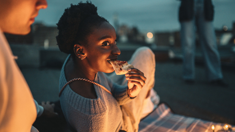 Woman eating pizza on a picnic blanket at night