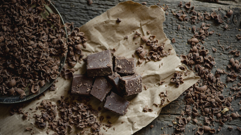 Chocolate pieces and shavings on a piece of brown paper on a textured stone table