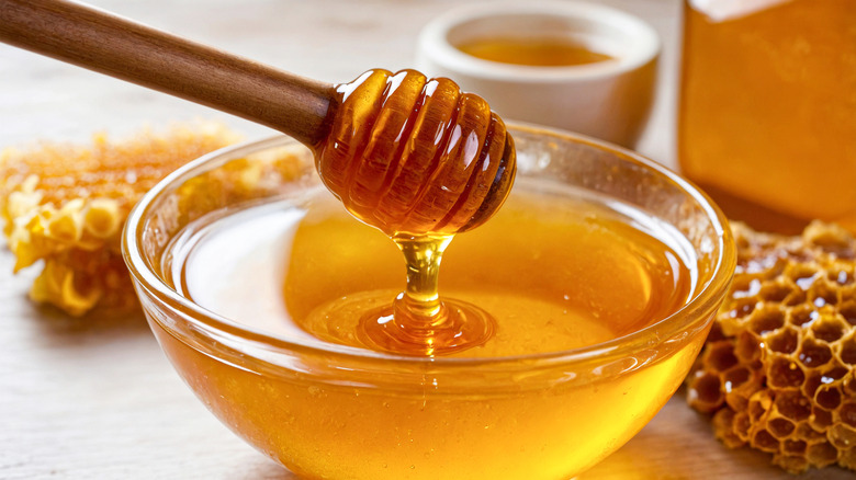 A honey stick drips honey into a bowl of golden honey