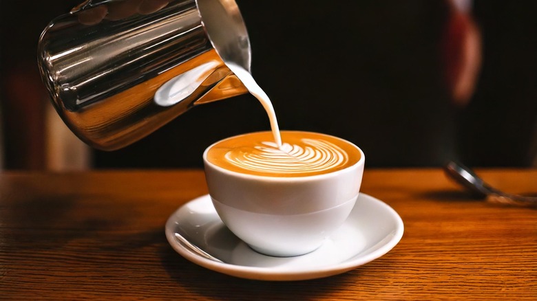 Pouring milk into latte cup with art