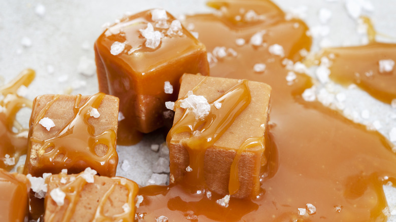 Cubes of caramel with a caramel drizzle and flaky salt on a white table