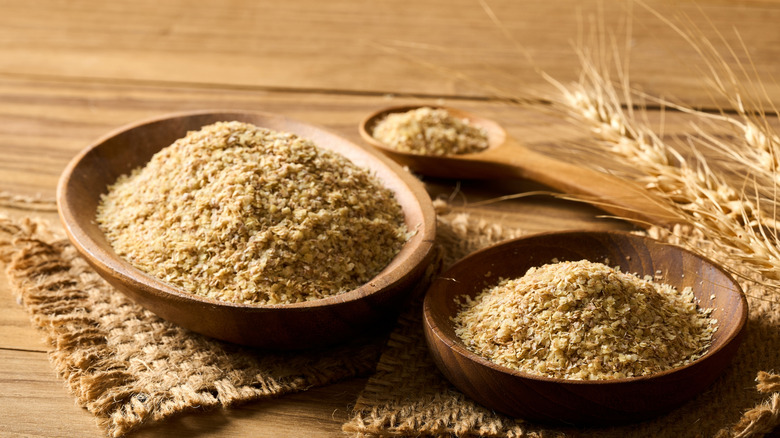 Wooden bowls of wheat germ on brown woven mats with wheat stalks and a spoon