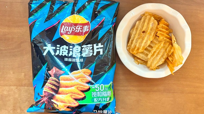 black and blue Grilled Squid chip bag next to a white bowl of chips