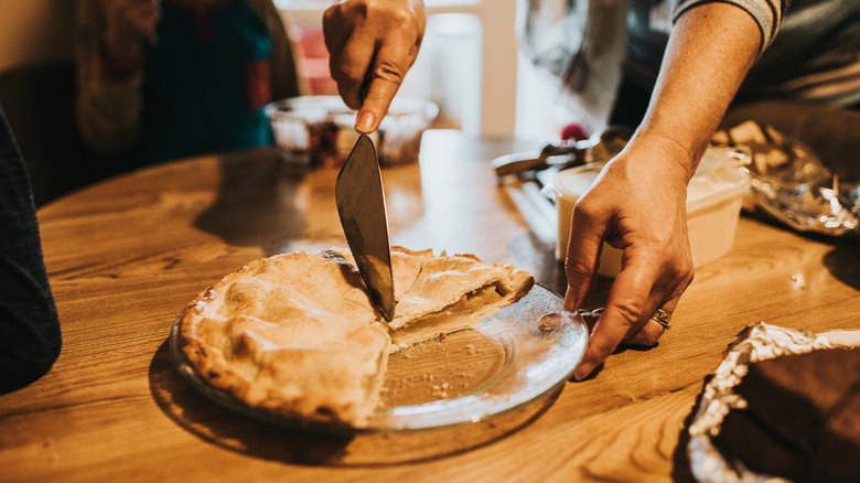 Hand slicing into apple pie on table