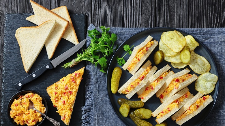 Pimento cheese sandwiches served with pickles and chips on a black plate