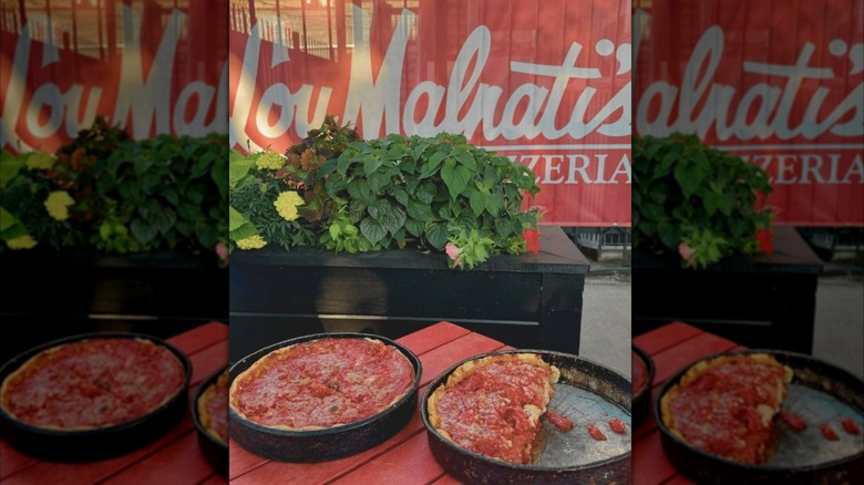 Two pizzas in front of Lou Malnati's sign