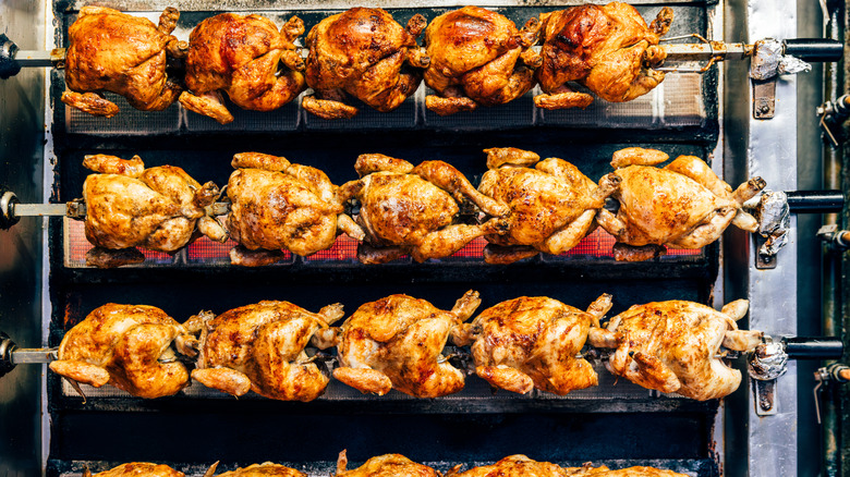 rows of rotisserie chickens roasting on spits