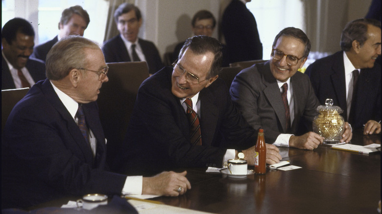 George H.W. Bush talks to House Speaker James C. Wright and Sen George J. Michaels with hot sauce and pork rinds at the desk